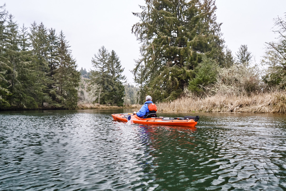 A person kayaking on a narrow river.