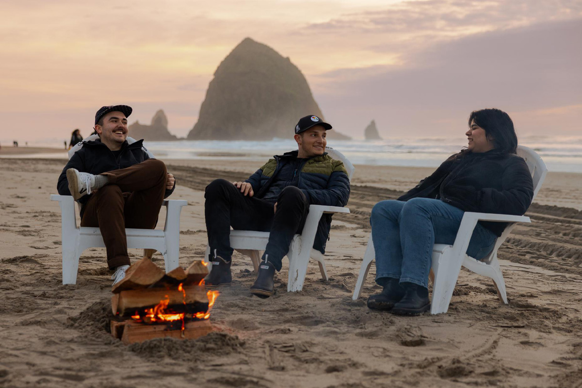 A group of people sitting around a campfire on the beach.