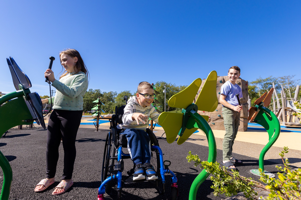A child in a wheelchair interacting with a flower sculpture in a kid's playground.